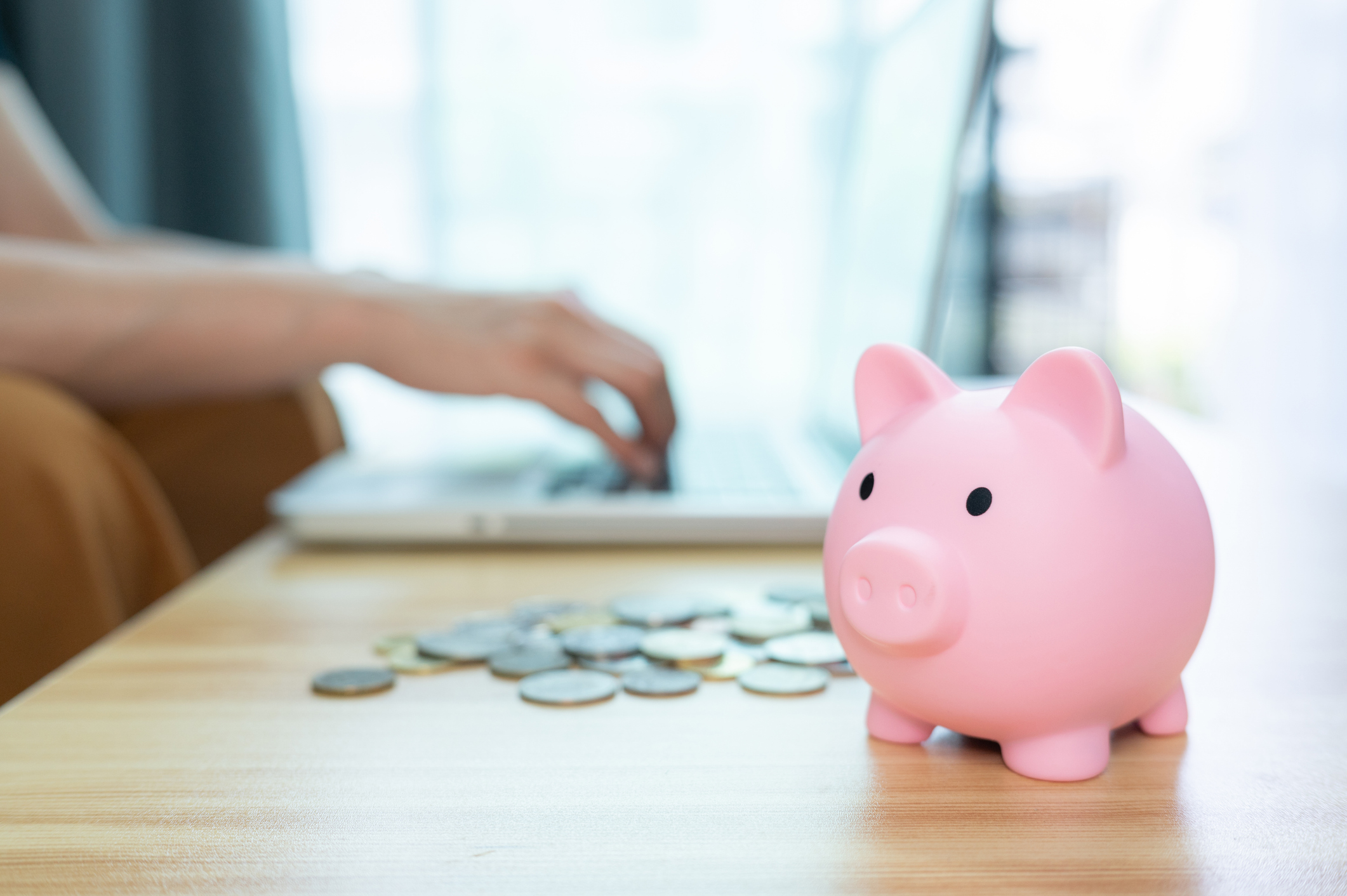 A pink piggy bank on table with someone working on laptop in the background